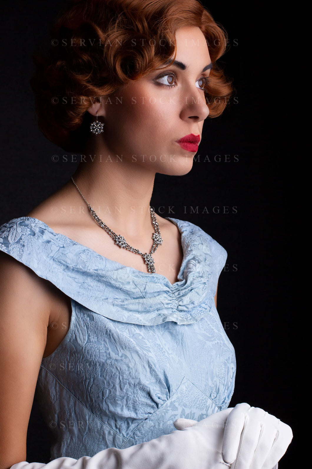 1930s woman wearing a blue vintage dress, long white gloves, and a diamante necklace against a black backdrop.(Sarah 0238)