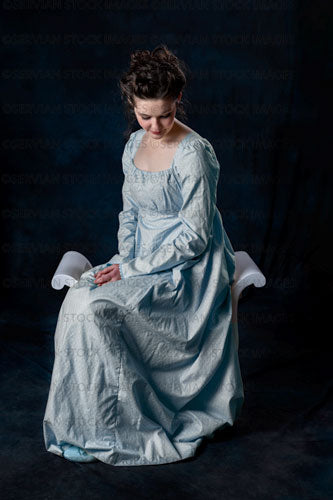 Regency woman wearing a blue cotton dress and sitting on a wooden seat (Brigit 8577)