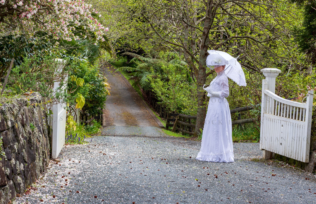 Edwardian woman in a white lace blouse and skirt holding a parasol and walking in a garden (Tayla 0183)