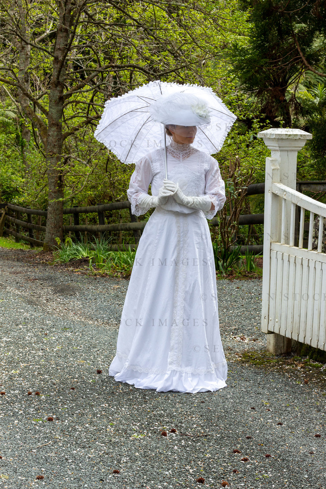 Edwardian woman in a white lace blouse and skirt holding a parasol and walking in a garden (Tayla 0187)