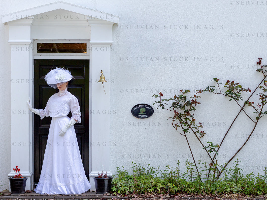 Edwardian woman in a white lace blouse and skirt and standing beside a cottage (Tayla 0288)
