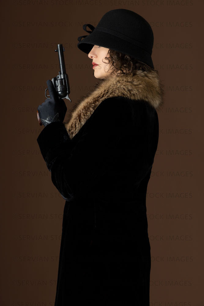 1920s woman holding a gun and wearing a black velvet coat and cloche hat (Emma 272)